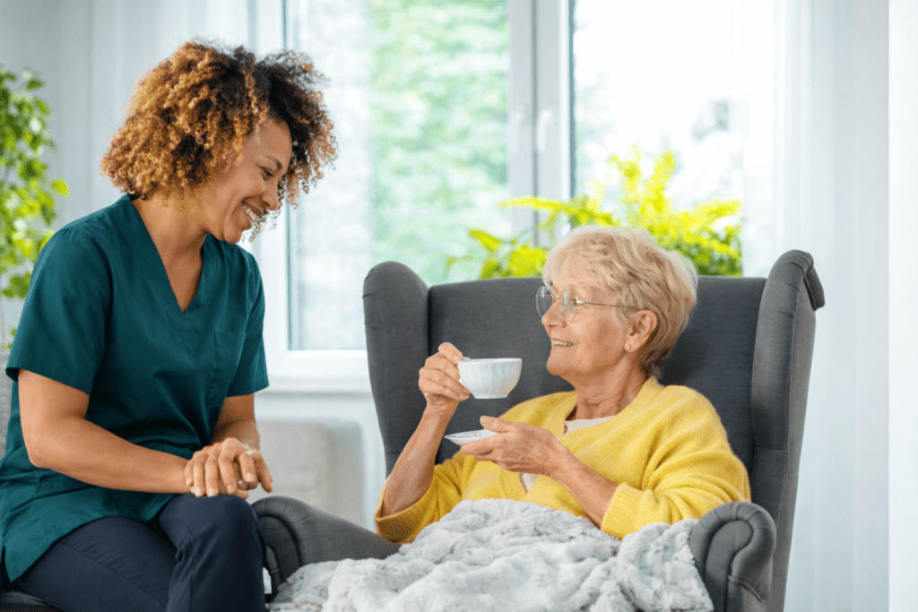 Caregiver sitting beside elderly person holding a teacup at home