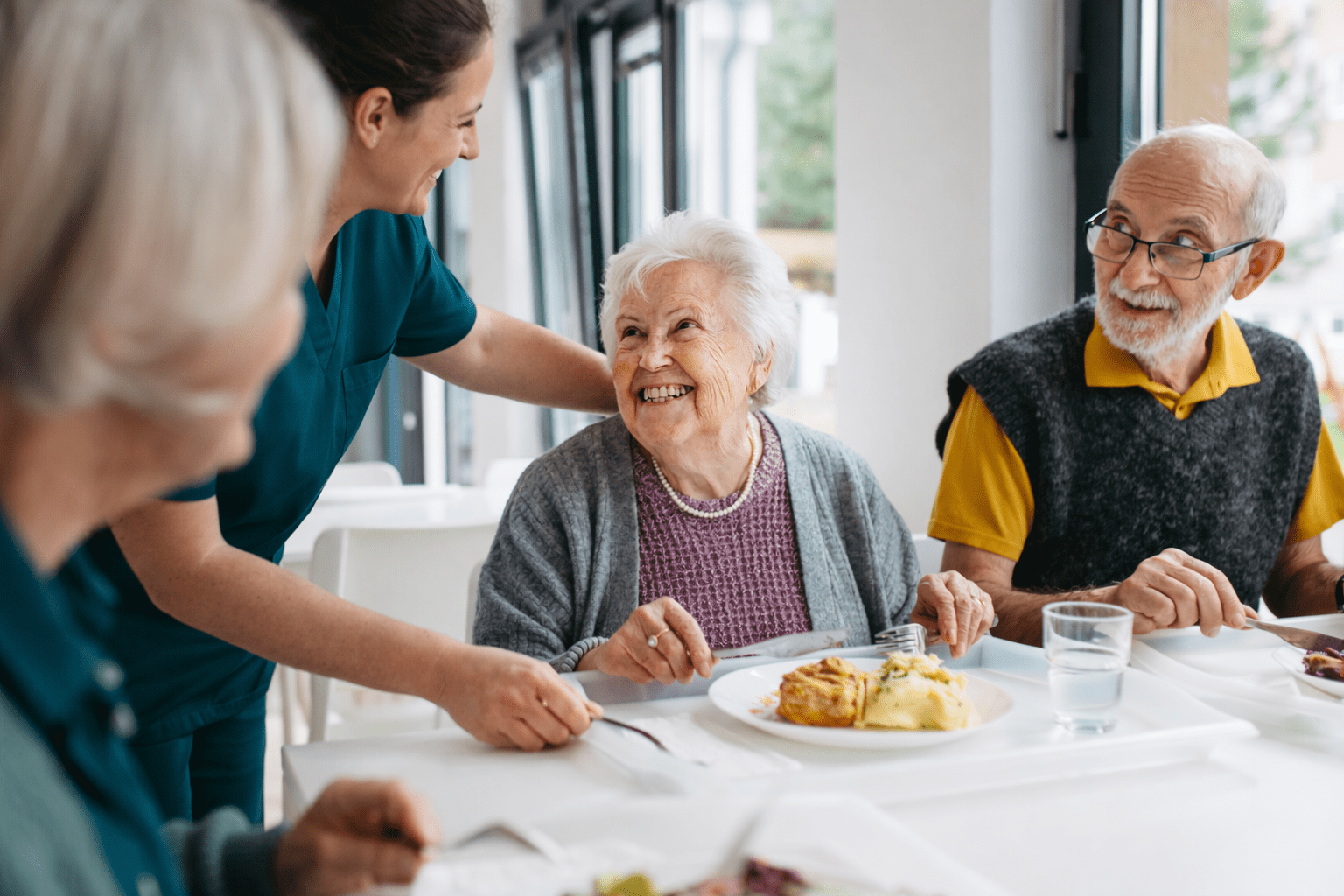 Healthcare worker assisting elderly residents at a dining table in a residential care setting