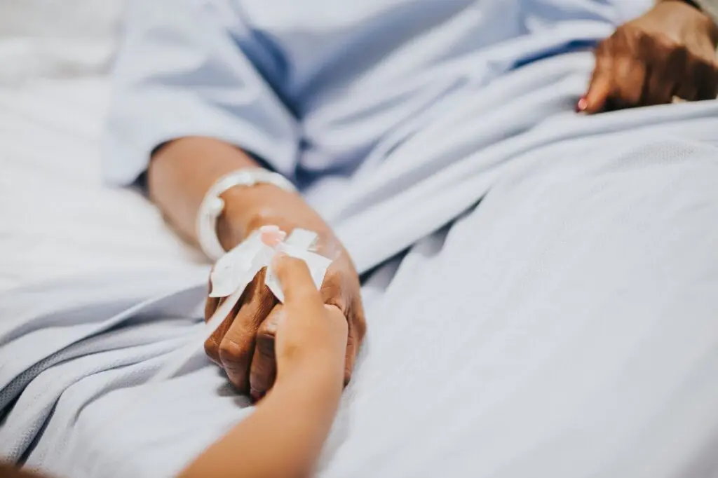 Healthcare worker holding a patient’s hand in bed, providing end-of-life care support