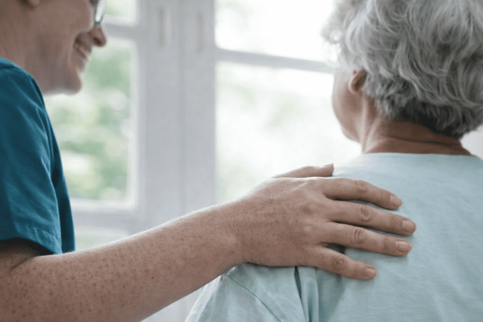 Nurse smiling while supporting a patient with a reassuring hand on their back