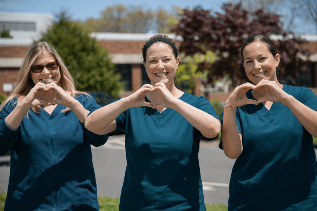 Three healthcare workers outdoors smiling and making heart shapes with their hands